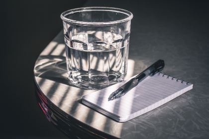 Sunlight shines on a glass of water next to a pad of paper and a pen. (iStock photo)